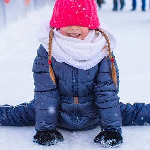 Young girl doing the splits in the snow wearing a bright pink hat